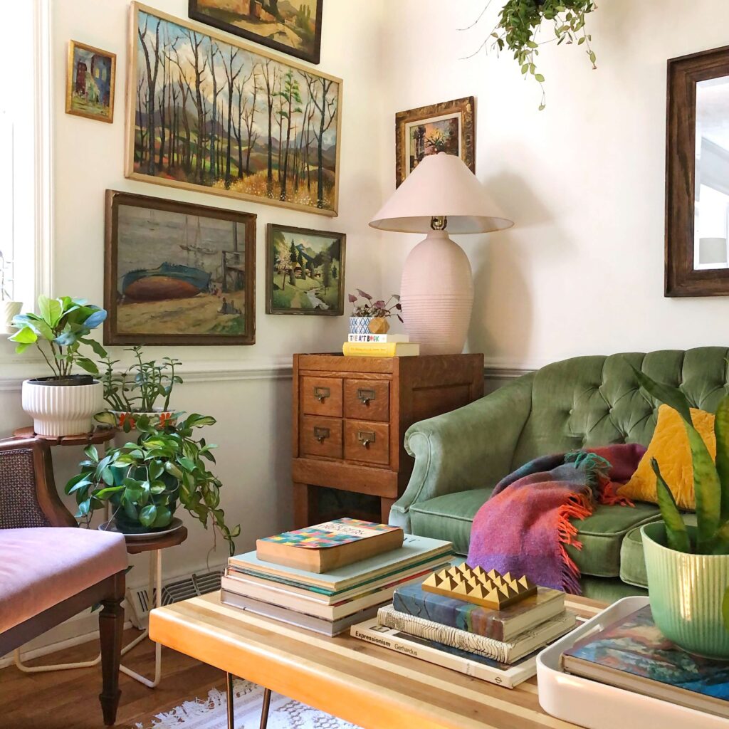 This living room corner has vintage artwork of landscapes, a green couch and a wooden side table.