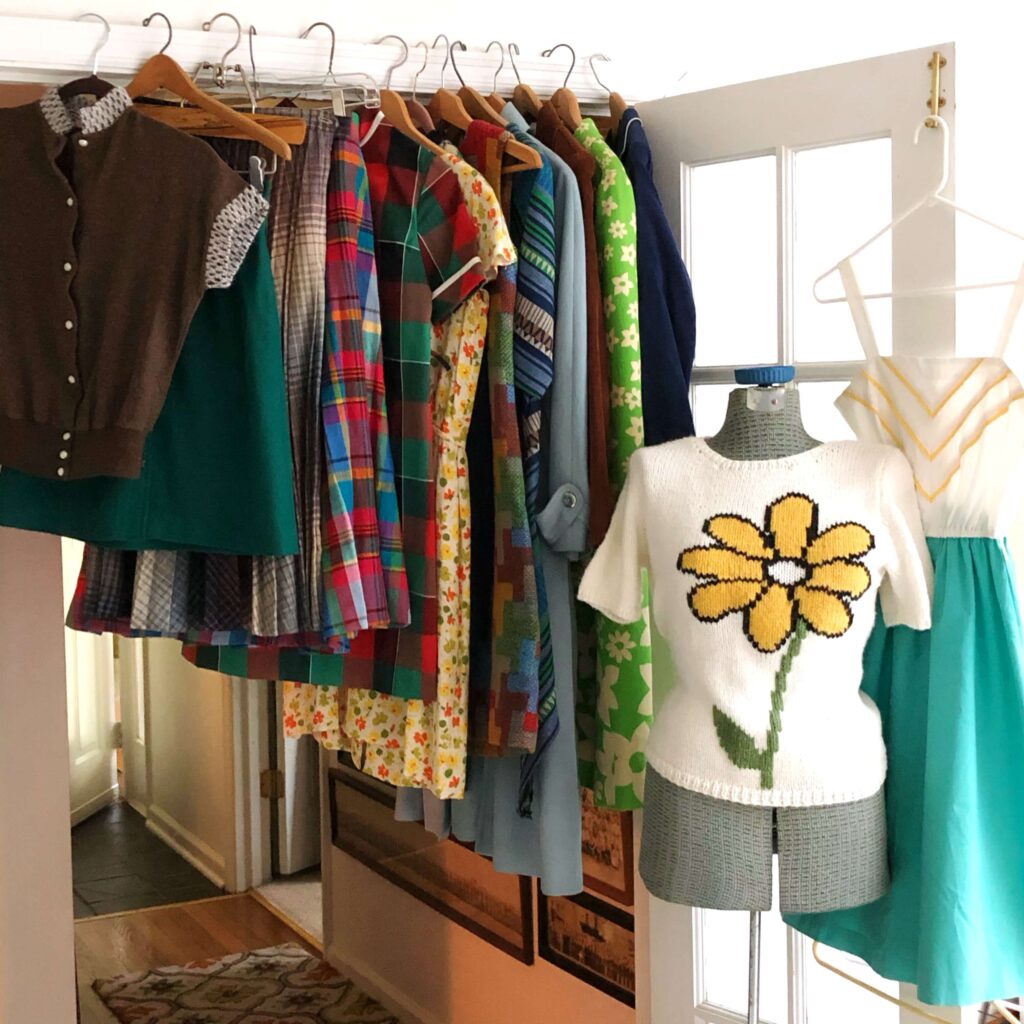 Vintage clothing hangs on a doorway, and a manikin displays a white sweater with a yellow flower.